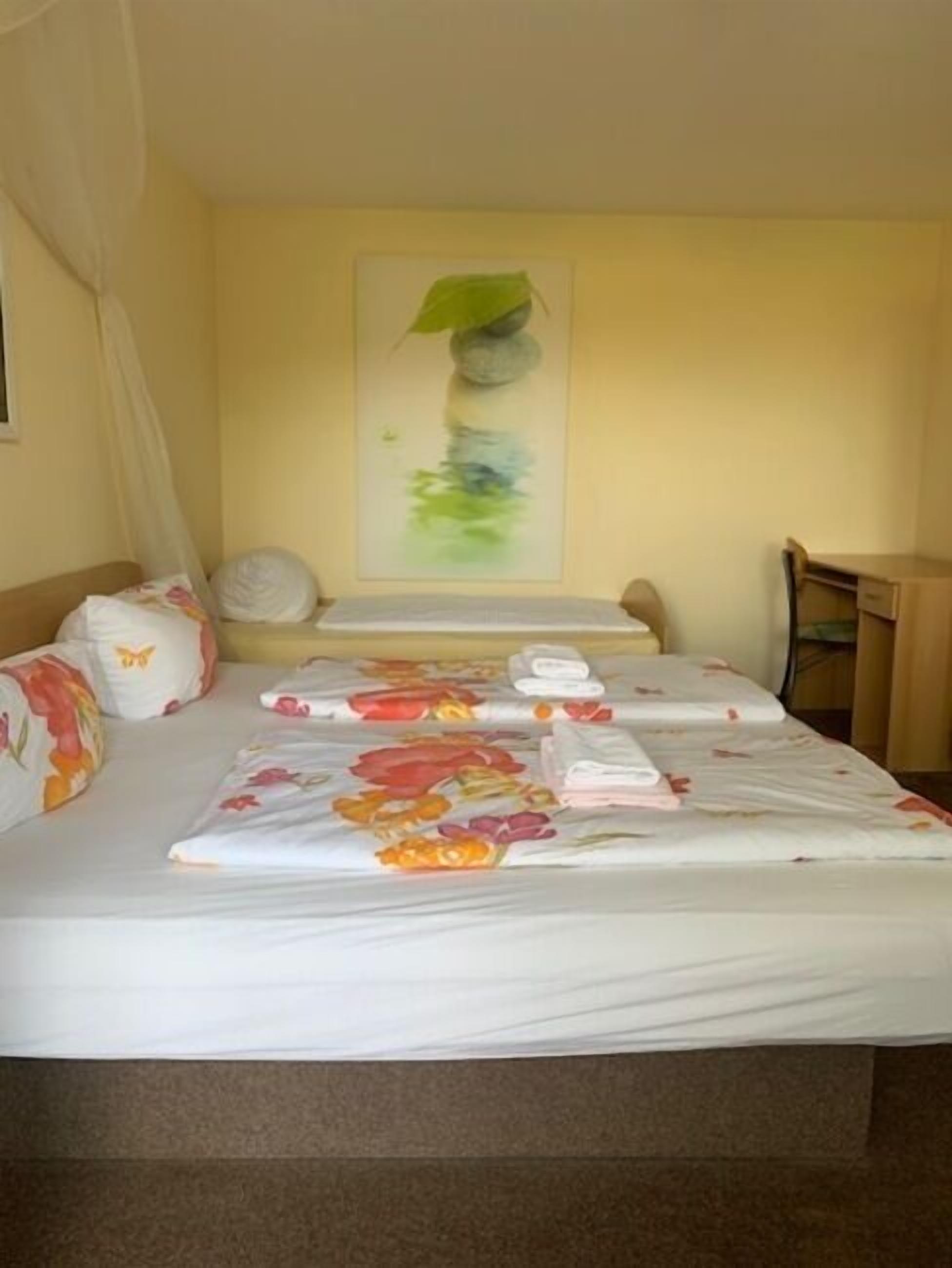 A hotel room with a bed, a desk, and a painting on the wall.