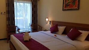Een hotelkamer met een bed, bureau, twee stoelen, raam met gordijnen, wandlamp en een schilderij.