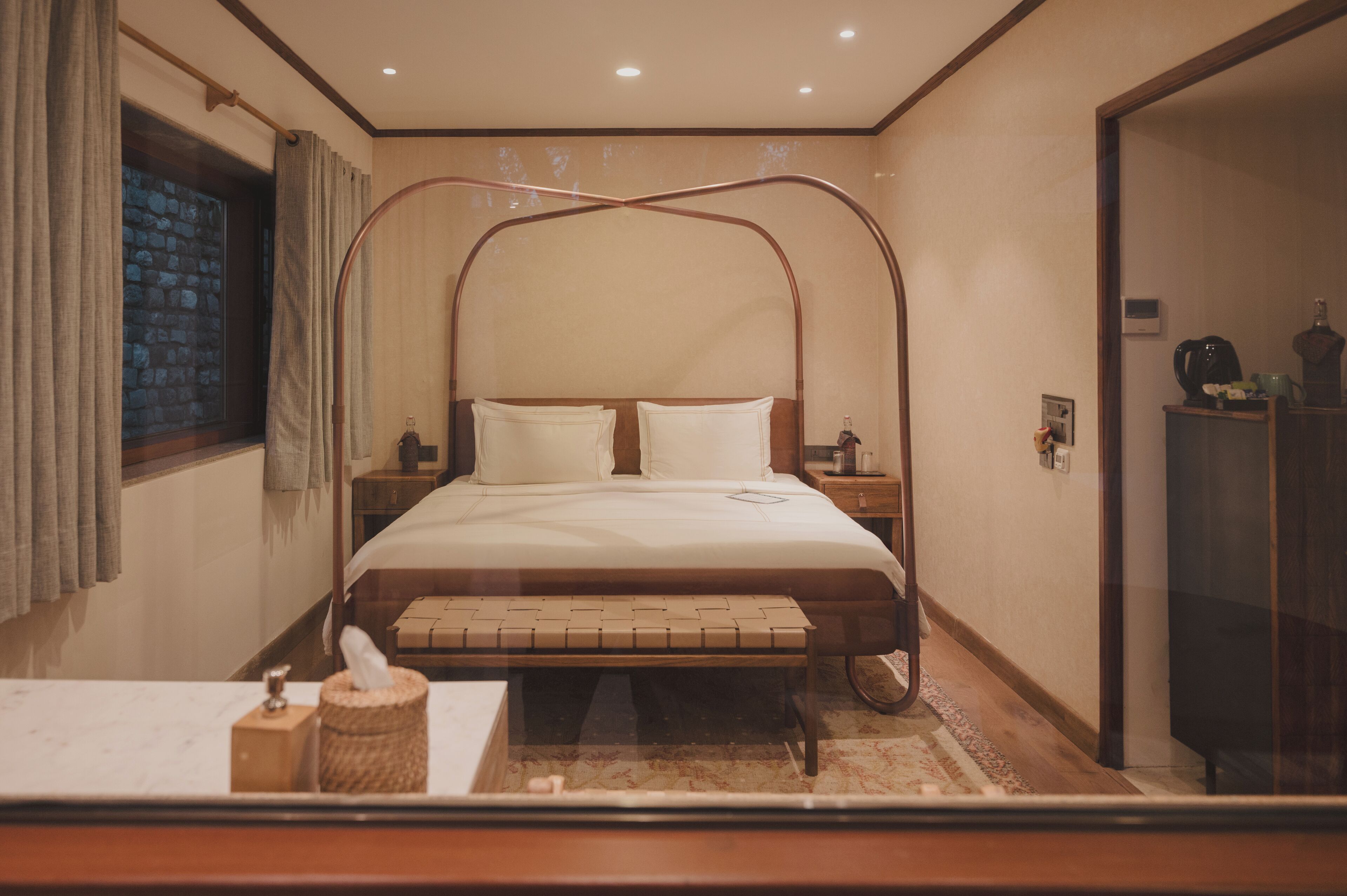 A neatly arranged bedroom with a four-poster bed, bedside tables, a bedside lamp, and a small bench.