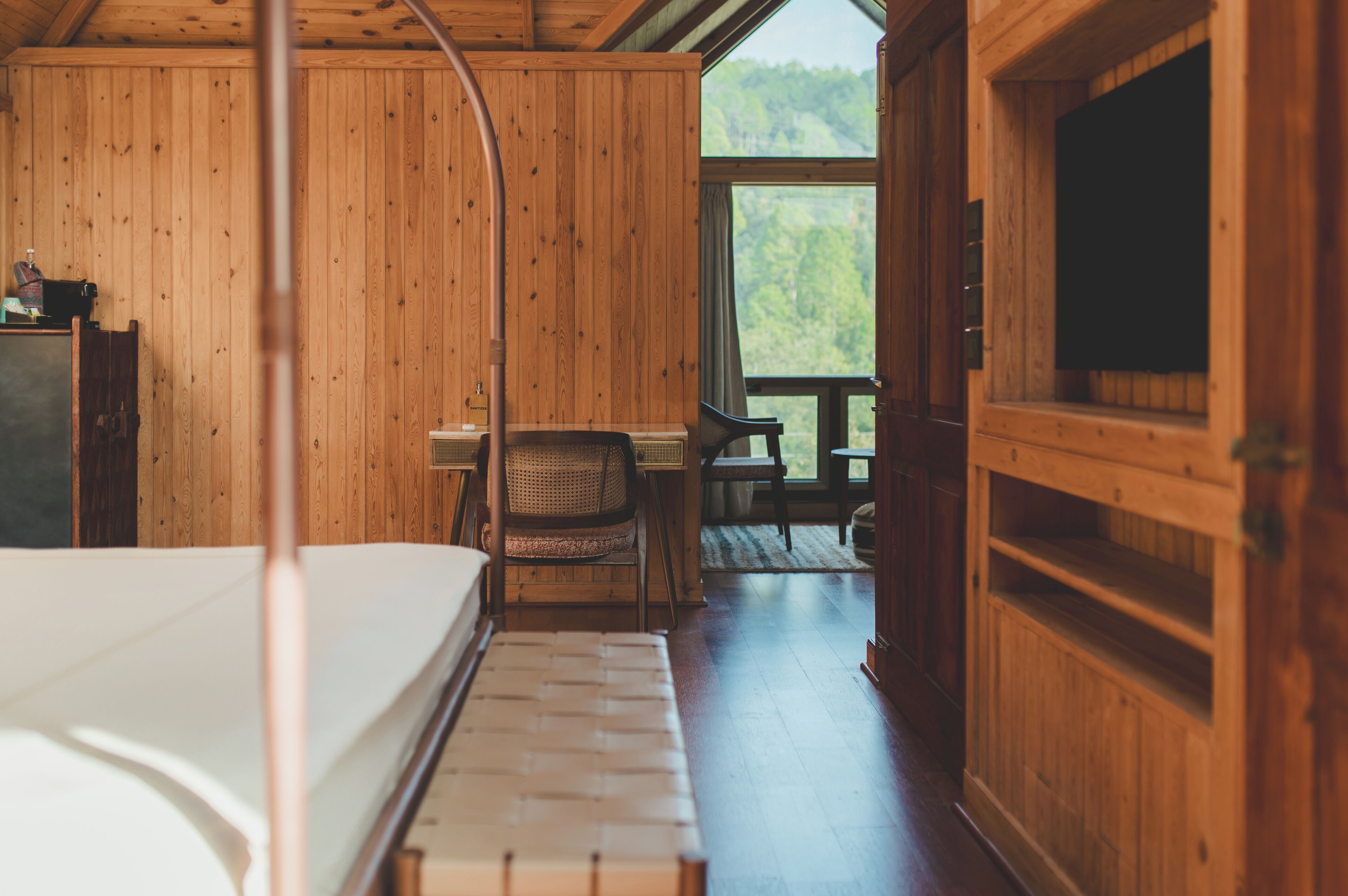 A wooden cabin interior with a bed, a desk, and a chair.