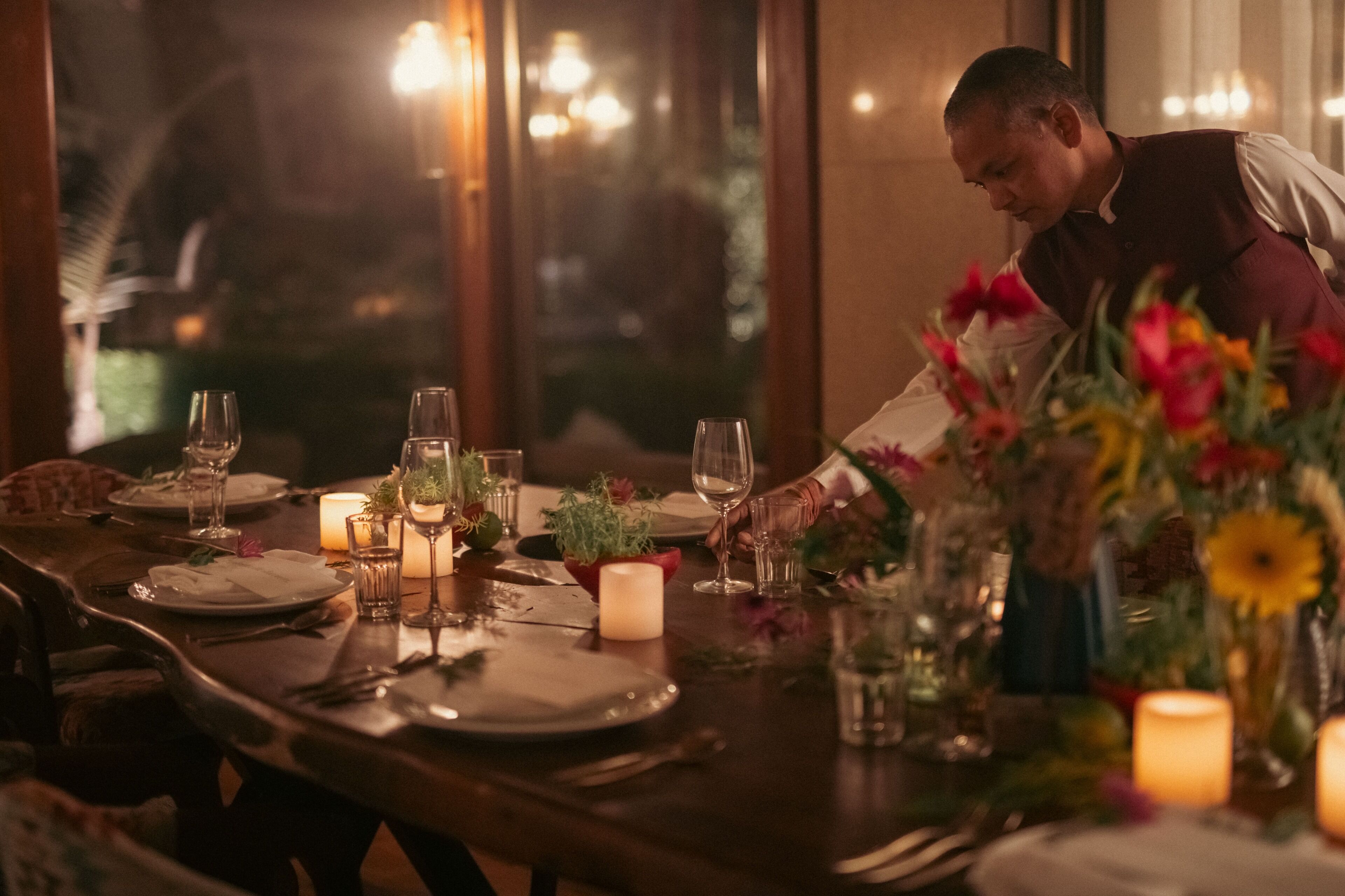 A dining table set for a meal with candles, glassware, and a floral centerpiece.