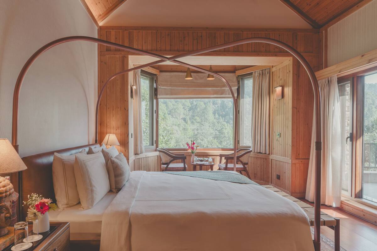 Une chambre avec un grand lit, des murs en bois, une fenêtre et une table avec des chaises.