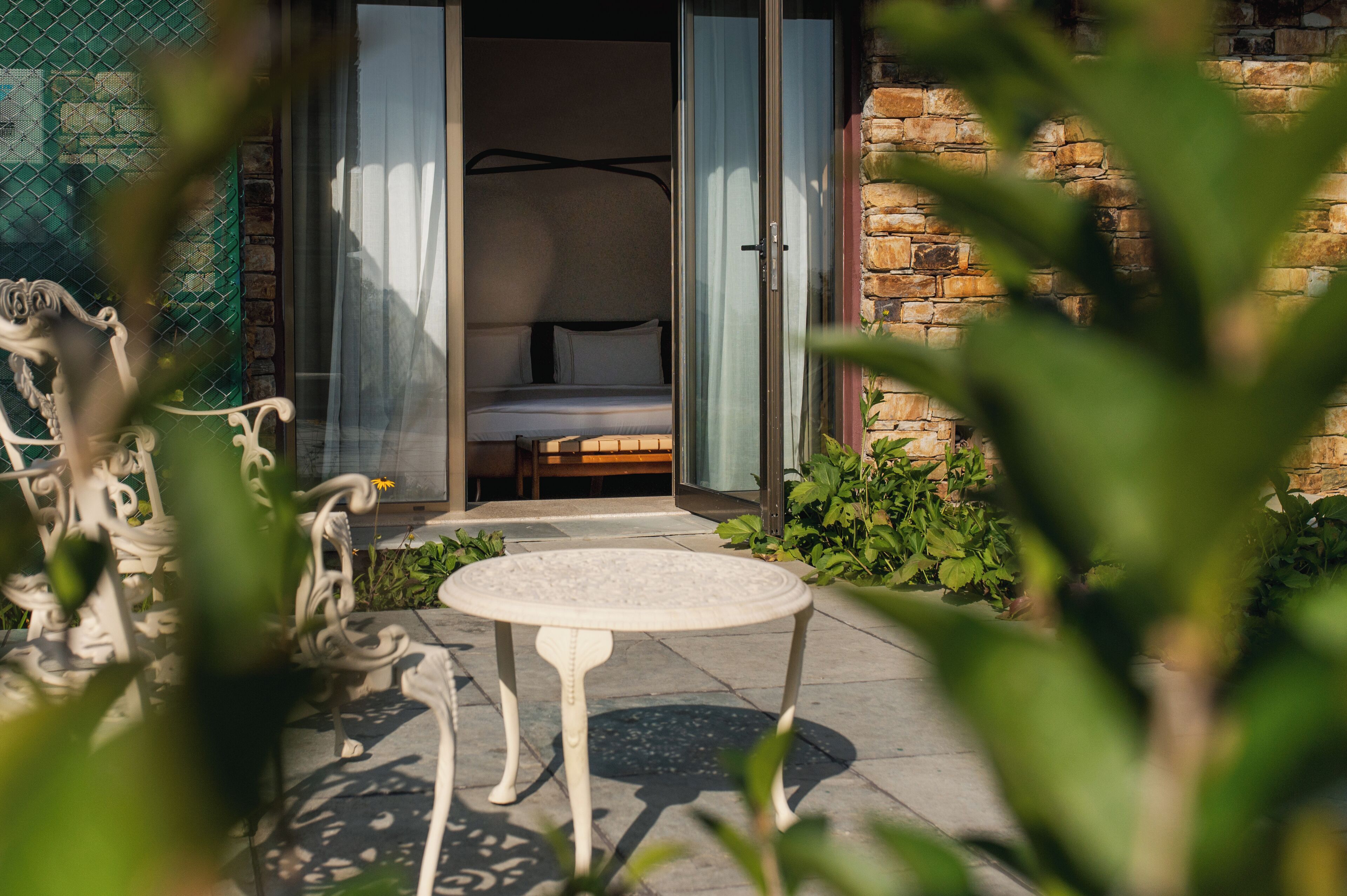 A room with a bed, a small table, and a view of a garden.