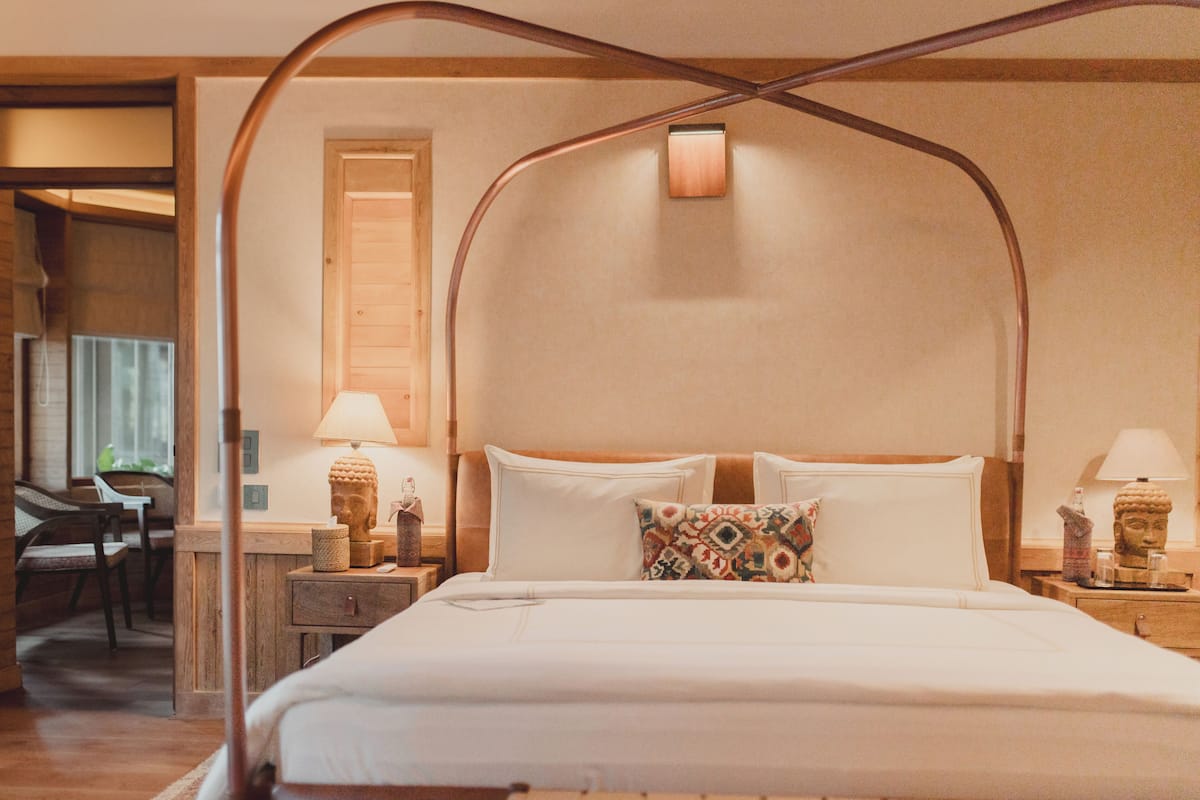 Une chambre d’hôtel avec un grand lit, une tête de lit en bois, deux tables de chevet avec des lampes et une petite statue sur chaque table.