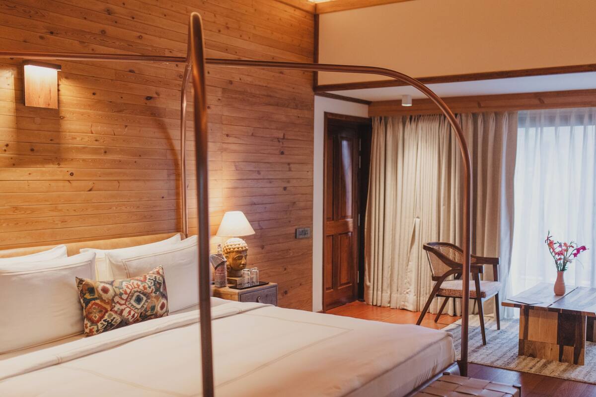 Une pièce aux murs lambrissés, comprenant un lit, une table de chevet avec une lampe, une chaise et une table sur laquelle est posé un vase de fleurs.