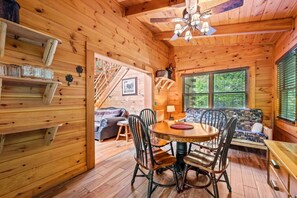 Ein gemütliches Blockhaus-Interieur mit Holztisch, Stühlen, einer Couch und einer Treppe zu einer erhöhten Ebene.