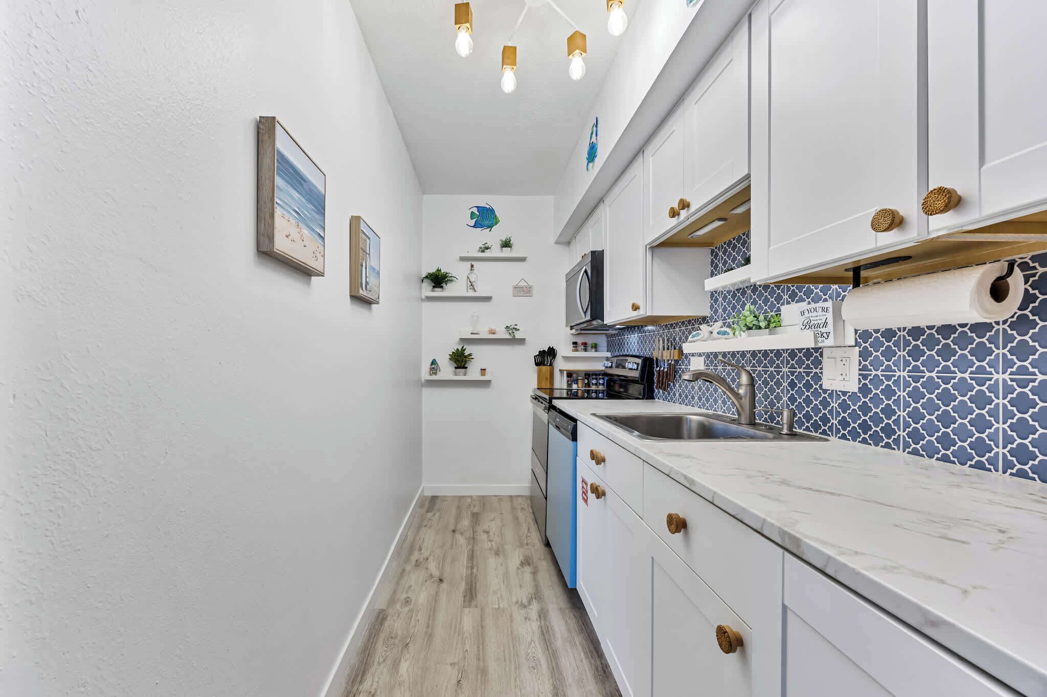 Una cocina estrecha con armarios blancos, un salpicadero azul y suelo de madera.