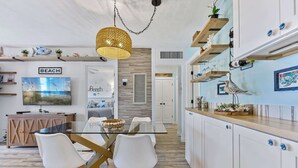 Une cuisine moderne avec des meubles blancs, une table à manger en verre et un luminaire suspendu.