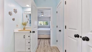 Un couloir étroit avec un lit au centre, des portes blanches et un ventilateur de plafond.
