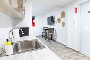 A modern kitchen with a sink, a dining area with chairs, a flat-screen TV, and a fire extinguisher.