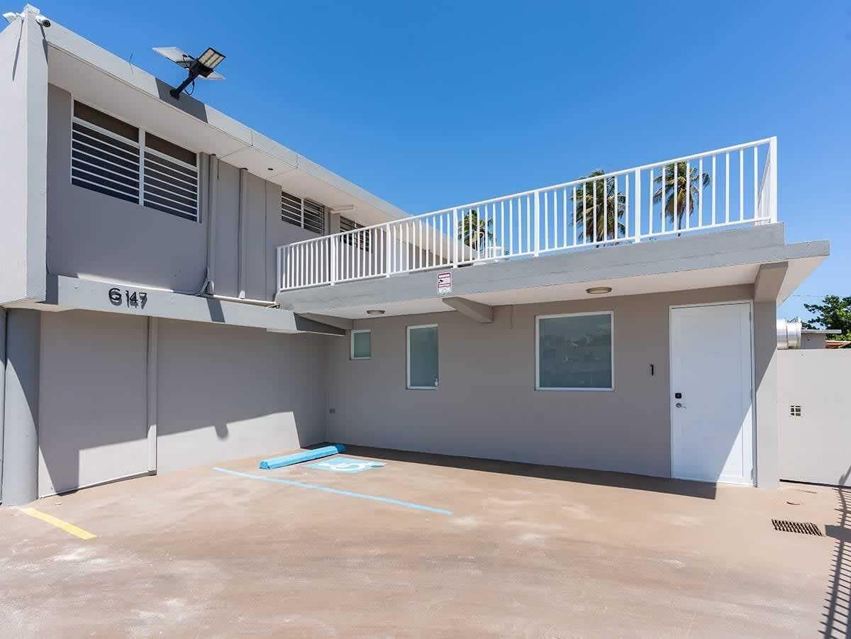 A two-story building with a balcony, a garage door, and a clear sky.