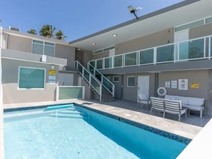 A modern building with a swimming pool, outdoor seating, and a staircase leading to an upper level.