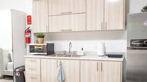 Une cuisine moderne avec des meubles de couleur bois clair, un réfrigérateur en acier inoxydable, un four à micro-ondes, un évier et un extincteur.