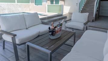 Un área de lounge en la azotea con piscina, sofás blancos y una botella de champán.
