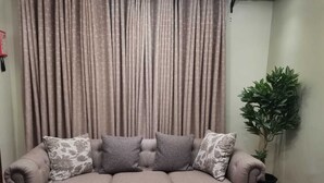 A grey three-seater sofa with floral cushions, a wooden coffee table, and a potted plant in a corner. - HAVEN STAY HOTEL (Eldoret)