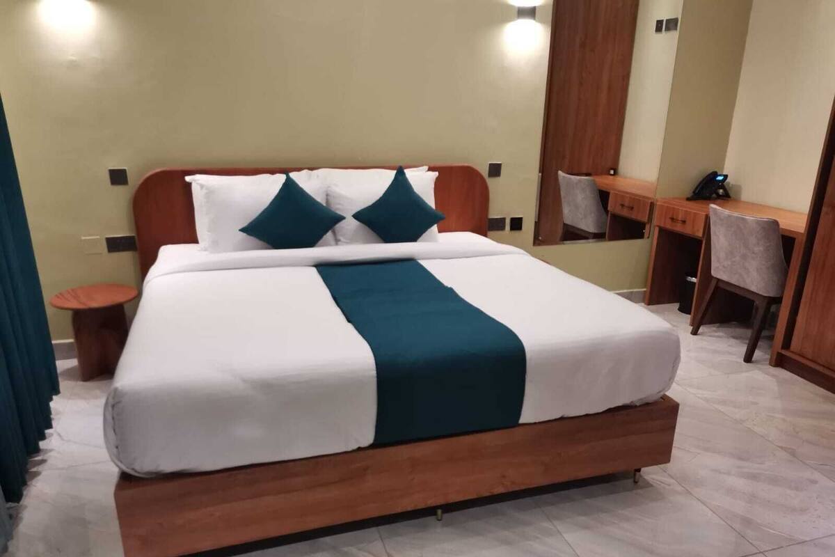Uma cama bem arrumada com colcha branca e azul-turquesa, uma cabeceira de madeira e uma pequena mesa redonda ao lado.