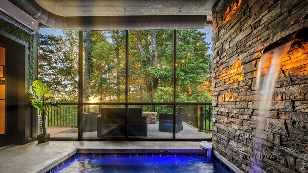 Una piscina interior moderna con una cascada, rodeada de amplios ventanales que ofrecen vistas a un área boscosa.