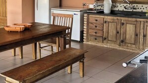 Een keuken met een houten tafel, stoelen, een koelkast, een gootsteen en een raam met uitzicht op groen.