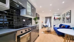 Una cocina moderna con salpicadero de azulejos negros, electrodomésticos de acero inoxidable y una zona de comedor con sofá azul y mesa blanca.