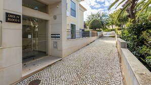A building with a sign reading "LOTE 79 BLOCO E" and a cobblestone pathway leading to the entrance.