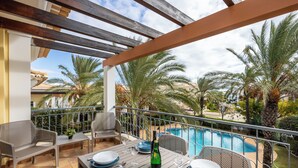 An outdoor dining area with a pool view, featuring a table set for two with plates, glasses, and a bottle.