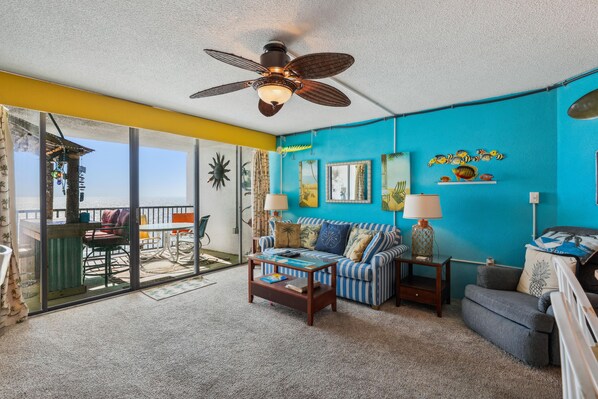 A room with a ceiling fan, a sofa, a coffee table, and a view of the ocean through large windows. - Includes Xplorie Activities & Linens. PYRAMID-1BR OF condo w/outdoor pool. (Ocean City)