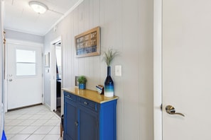 Um corredor com uma placa de madeira, um armário azul, um vaso de planta e uma porta com puxador de latão.