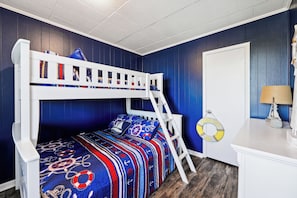 Una cama litera con escalera, un escritorio con lámpara y un círculo salvavidas en la pared.