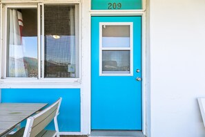 Une porte bleue avec le numéro « 209 » au-dessus, une fenêtre donnant sur un immeuble et un banc à l’extérieur.