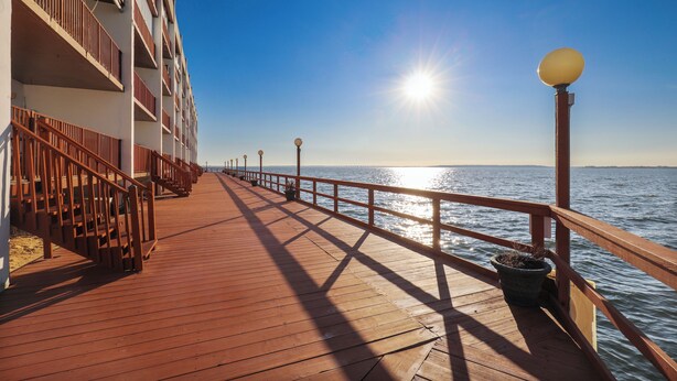 A wooden pier extending from a building with balconies, leading to a body of water. - Xplorie Activities and Linens Included. Great 2BR/2BA bayfront condo on 94th Street! (Ocean City)
