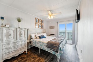 Een slaapkamer met een bed, een dressoir, een plafondventilator en uitzicht op het landschap.