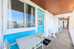 Een overdekt terras met een tafel en stoelen, een deur met een nummer en uitzicht op de stad door het raam.