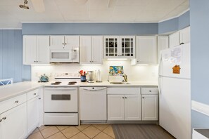 Une cuisine avec des meubles blancs, un four à micro-ondes, une cuisinière, un lave-vaisselle et un réfrigérateur.