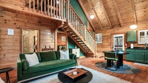 Interior acogedor de una cabaña con un sofá verde, una mesa de comedor y una escalera que sube a un nivel superior.