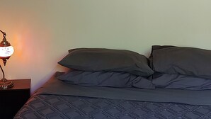 Un dormitorio con cama, almohadas, una mesita de noche y una lámpara de pared.