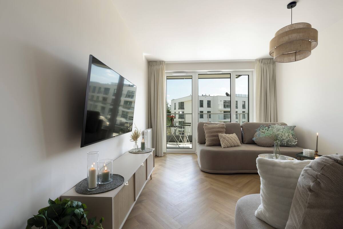 A modern living room with a flat-screen TV, a sofa, a coffee table, and a large window with curtains.