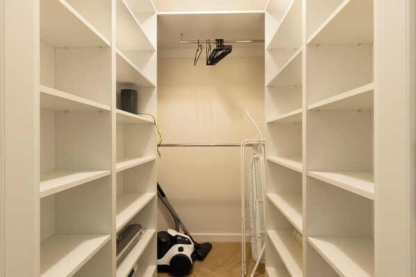 Un vestidor con estantes blancos, un aspirador y un tendedero.