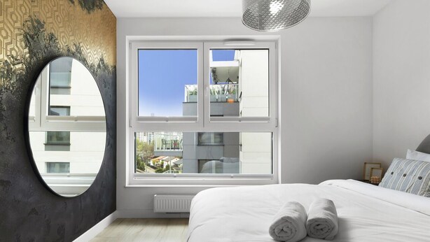 Ein modernes Schlafzimmer mit einem großen Bett, einem runden Spiegel und einem Fenster mit Blick auf die Stadt.