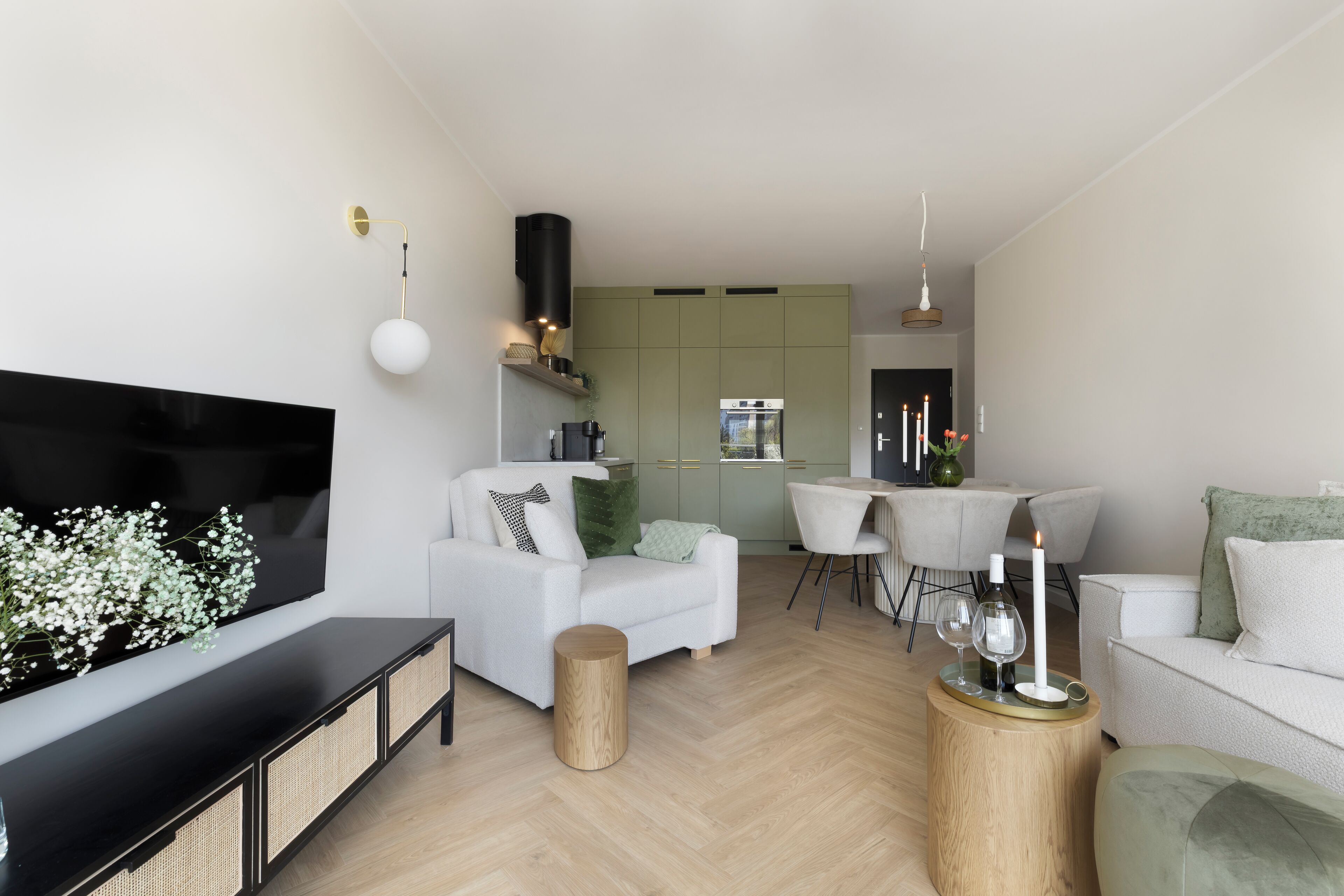 Een moderne woonkamer met een flatscreen televisie, een bank, een eettafel en een keuken op de achtergrond.