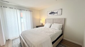 A neatly arranged bedroom with a bed, a nightstand, a lamp, and a painting on the wall. - Nice condo in the heart of Rehoboth! (Rehoboth Beach)