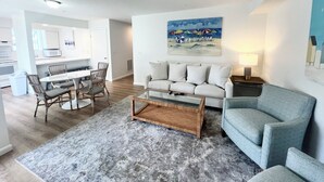 A modern living room with a grey sofa, a coffee table, and a dining area with chairs and a table. - Nice condo in the heart of Rehoboth! (Rehoboth Beach)