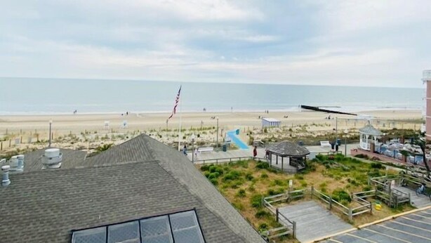 A beach view from a hotel with a parking area, a gazebo, and a flag.