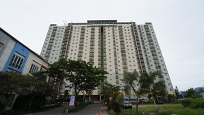 A high-rise hotel with multiple balconies, a gated entrance, and a landscaped area with trees and a pathway. - Hotel O Metro Suite Apartment By Pian (Bandung)