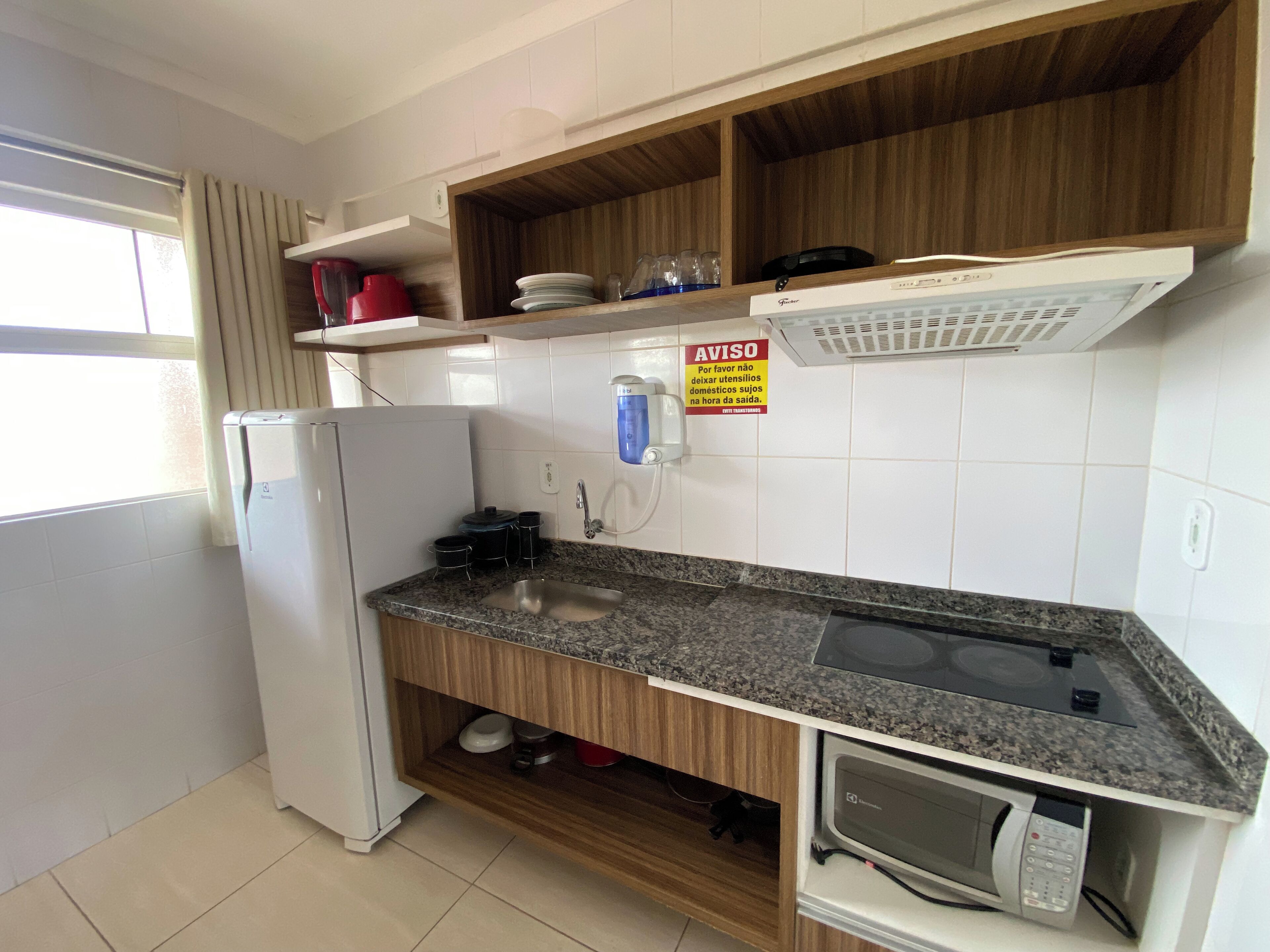 Una cocina compacta equipada con refrigerador, microondas, lavamanos y estantes de madera.