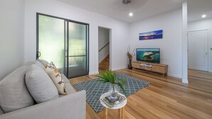 Ein modernes Wohnzimmer mit einer Couch, einem Couchtisch mit einer Zeitschrift, einem Fernseher auf einem Holzständer und einem Bild an der Wand.