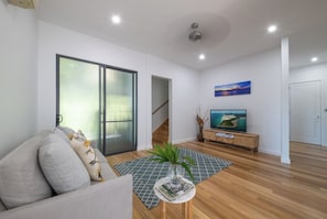 A modern living room with a sofa, a coffee table with a magazine, a TV on a wooden stand, and a painting on the wall. - Airlie Nights (Airlie Beach)