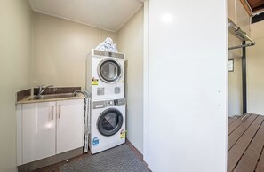 A laundry area with stacked washing machines, a sink, and cabinets. - Airlie Nights (Airlie Beach)