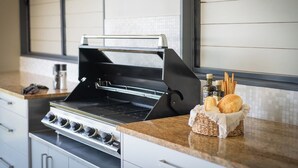Eine Küche mit integriertem Grill, einer Arbeitsplatte mit einem Brotkorb und einem Fenster mit Jalousien.