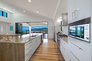 A modern kitchen with a large island, stainless steel appliances, and a view to the outdoors. - Airlie Nights (Airlie Beach)