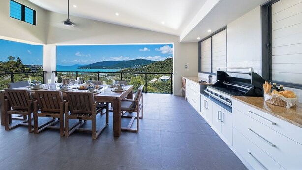 Eine moderne Küche mit Meerblick, ein Essbereich mit Holzmöbeln und ein Balkon mit schöner Aussicht.
